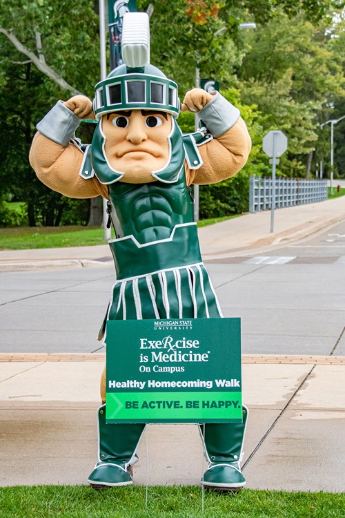 The Sparty mascot behind a sign which reads 